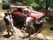 1995 Ford C-350 (Centurion Conversions) - People are working on a red pickup truck off-road, with another vehicle in the background.