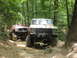 1995 Ford C-350 (Centurion Conversions) - Two lifted Ford trucks navigate a rocky, wooded trail during an off-road event.