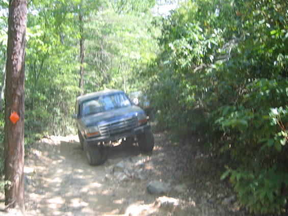 Dark SUV with large tires on a rocky, wooded trail