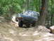 1995 Ford C-350 (Centurion Conversions) - Two trucks navigate a challenging rocky trail in a wooded area during an off-road event.