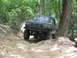 1995 Ford C-350 (Centurion Conversions) - Blue SUV navigating a challenging rocky trail in a wooded area.