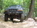 1995 Ford C-350 (Centurion Conversions) - Two Ford trucks drive on a wooded trail, one in front with large tires and a bull bar.
