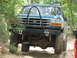 1995 Ford C-350 (Centurion Conversions) - A green Ford F-Series truck navigates a rocky trail, its front end a prominent brush guard and off-road tires.