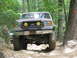 1995 Ford C-350 (Centurion Conversions) - This modified Ford F-Series truck navigates a challenging off-road path through a wooded area.