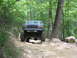 1995 Ford C-350 (Centurion Conversions) - A lifted Ford truck navigates a challenging, rocky path through a wooded area.
