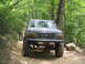 1995 Ford C-350 (Centurion Conversions) - This lifted 1995 Ford C-350 (Centurion Conversions) navigates a rough dirt trail in a wooded area.