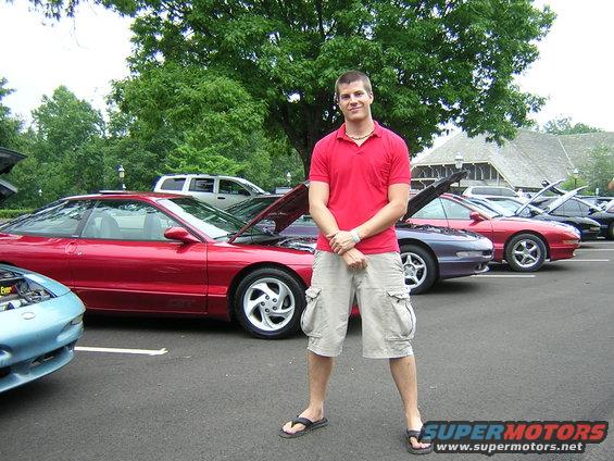 Man in red polo and cargo shorts stands in front of a line of parked Ford Probe cars