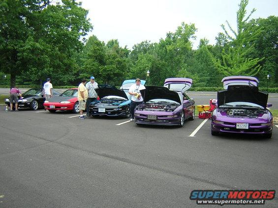 Four purple Ford Probes parked in a lot, hoods open, with people around them