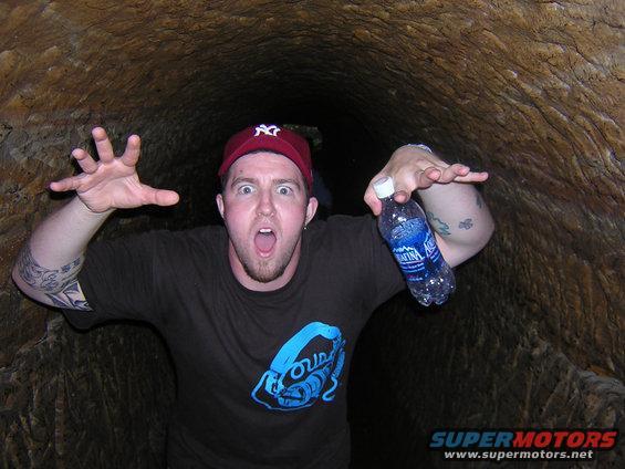 Man with surprised expression and outstretched hands holds a water bottle inside a tunnel