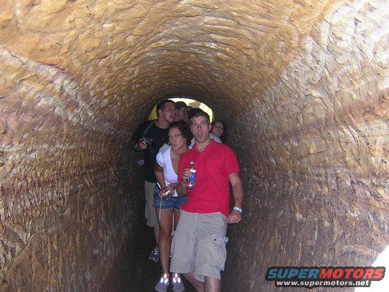 Group of people walking through a rough-hewn tunnel, one man in a red shirt in the foreground