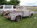 1955 Ford F-100 - A weathered pickup truck sits beside a white SUV, both appearing to be in disrepair.