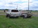 1955 Ford F-100 - A white SUV and a light blue pickup truck sit in a grassy field, both showing signs of age and rust.