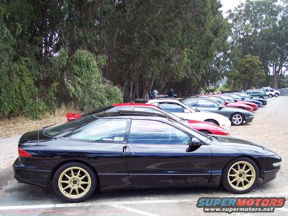 Black 1995 Ford Probe with gold rims parked in a line of cars