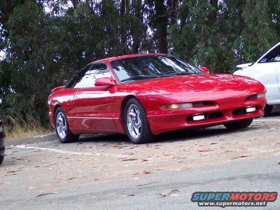 1995 Ford Probe parked on gravel lot with trees in background. Another white vehicle is partially visible on the right