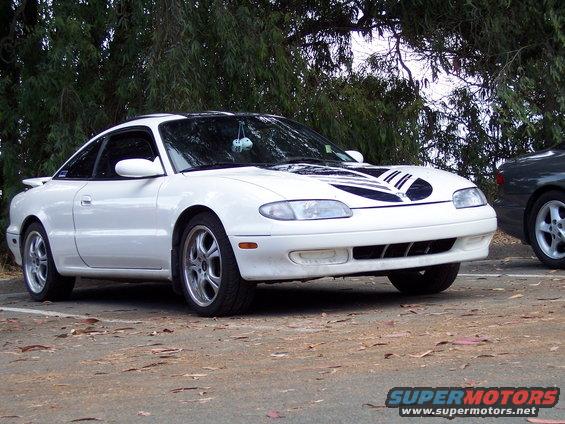 White Mazda MX-6 with black racing stripes on the hood parked outside
