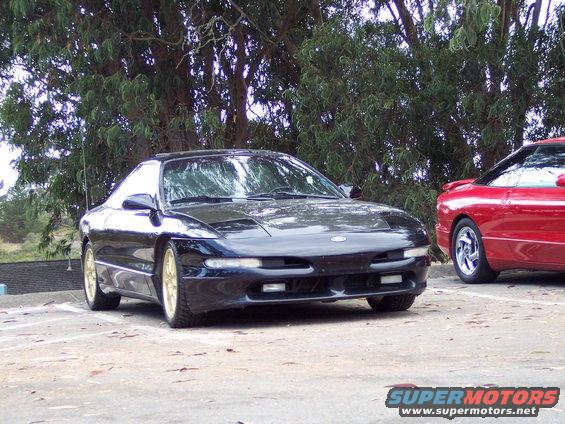 Black Ford Probe with gold wheels parked next to a red Ford Probe