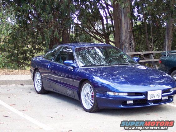Blue Ford Probe parked outside with trees and a picnic table. Another car is visible to the right