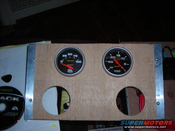 Wooden panel with two gauges, one for oil pressure and one for vacuum, and two circular cutouts