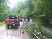 1995 Ford C-350 (Centurion Conversions) - A group of people stand around a modified red Ford Bronco on a dirt road in a wooded area.
