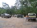 1995 Ford C-350 (Centurion Conversions) - A group of off-road vehicles and people gathered in a wooded area.