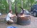 1995 Ford C-350 (Centurion Conversions) - A man cooks over a campfire at a campsite, with tents and a vehicle nearby.