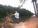 1995 Ford C-350 (Centurion Conversions) - A young boy poses on a fallen tree near the water's edge, with a dense forest lining the opposite bank.