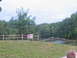 1995 Ford C-350 (Centurion Conversions) - A split-rail fence borders a grassy area leading to a lake, with a sign posted near the fence.