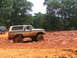 1995 Ford C-350 (Centurion Conversions) - A lifted Ford Bronco is stuck in a mud pit with trees in the background.