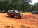 1995 Ford C-350 (Centurion Conversions) - Several vehicles are seen off-roading in a muddy area with trees in the background.