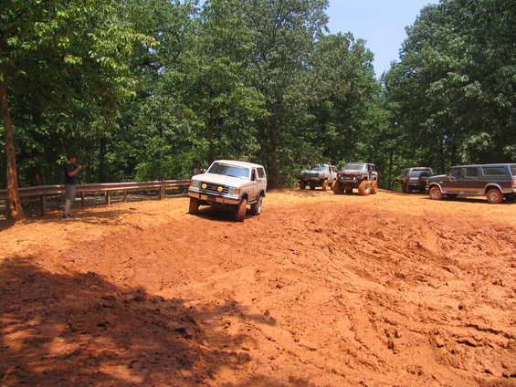 Several off-road vehicles parked on a muddy hill with trees in the background