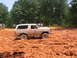 1995 Ford C-350 (Centurion Conversions) - A tan Ford Bronco navigates a muddy terrain, with spectators observing from a distance.