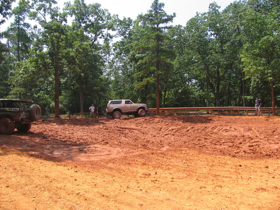 Tan Ford Bronco parked in mud with a spare tire on the back. Another vehicle is partially visible on the left