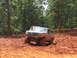 1995 Ford C-350 (Centurion Conversions) - A lifted Ford Bronco tackles a steep, muddy incline surrounded by trees.