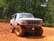 1995 Ford C-350 (Centurion Conversions) - A lifted Ford Bronco with mud-caked tires sits in a muddy off-road area.