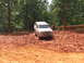 1995 Ford C-350 (Centurion Conversions) - A white SUV navigates a muddy trail, its off-road tires kicking up dirt.