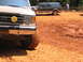 1995 Ford C-350 (Centurion Conversions) - A tan Ford F-Series truck sits in muddy terrain, with a dark SUV visible in the background.