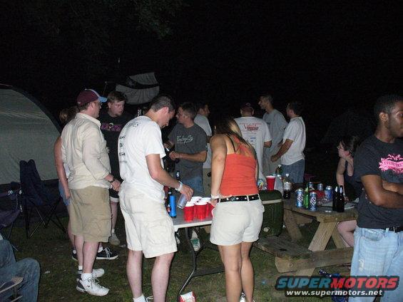 Group of people gathered around a picnic table with red cups and drinks at night