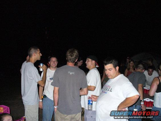 Group of people at a nighttime outdoor gathering, some holding drinks