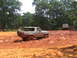 1995 Ford C-350 (Centurion Conversions) - A silver SUV is stuck in thick mud, with another truck visible in the background on a muddy trail.