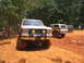 1995 Ford C-350 (Centurion Conversions) - Three off-road vehicles are parked on a dirt track with trees in the background.