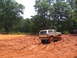 1995 Ford C-350 (Centurion Conversions) - A lifted Ford Bronco navigates a muddy off-road course with trees and a wooden fence in the background.
