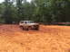 1995 Ford C-350 (Centurion Conversions) - A tan Ford Bronco navigates a muddy terrain with trees in the background.