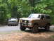 1995 Ford C-350 (Centurion Conversions) - Two trucks, a tan Ford Bronco and a green Ford F-Series, are parked on a dirt road surrounded by trees.