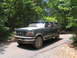1995 Ford C-350 (Centurion Conversions) - A dark green Ford truck with an extended cab sits on a paved road surrounded by trees.