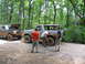 1995 Ford C-350 (Centurion Conversions) - Men work on off-road vehicles in a wooded area during an event.