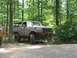 1995 Ford C-350 (Centurion Conversions) - A lifted Ford Bronco sits off-road in a wooded area, its front bumper removed.