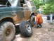 1995 Ford C-350 (Centurion Conversions) - A man kneels to change a flat tire on a muddy green Ford Bronco during an off-road event.