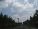 1995 Ford C-350 (Centurion Conversions) - A truck travels down a rural highway bordered by trees under a cloudy sky.