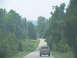 1995 Ford C-350 (Centurion Conversions) - A pickup truck travels down a country road surrounded by trees.