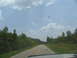 1995 Ford C-350 (Centurion Conversions) - Driving down a rural road with trees on either side and a single vehicle ahead.
